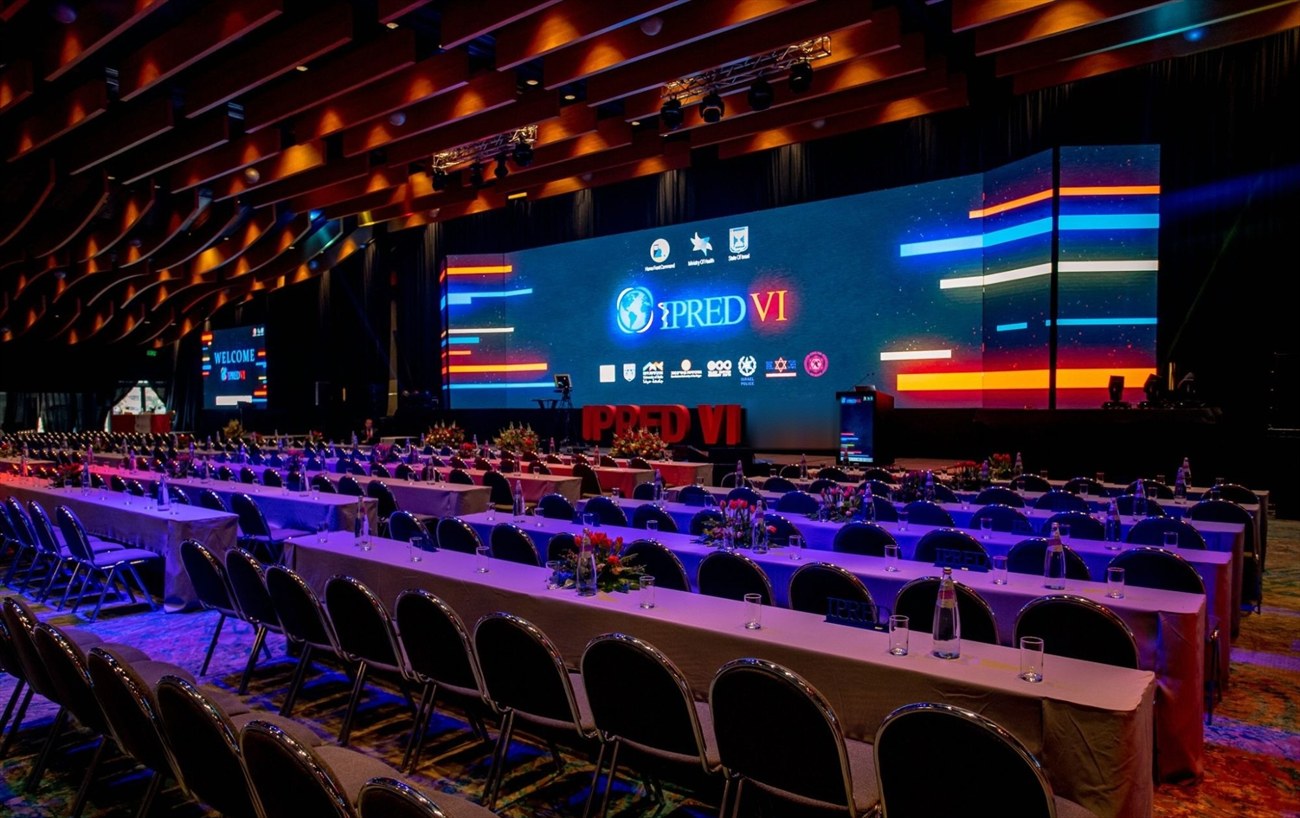 Banked tables under purple light facing a wide LED wall, the hall set and empty.