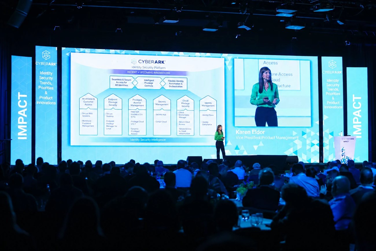 A speaker on the main stage beside a full width screen, the hall seated in front of it.