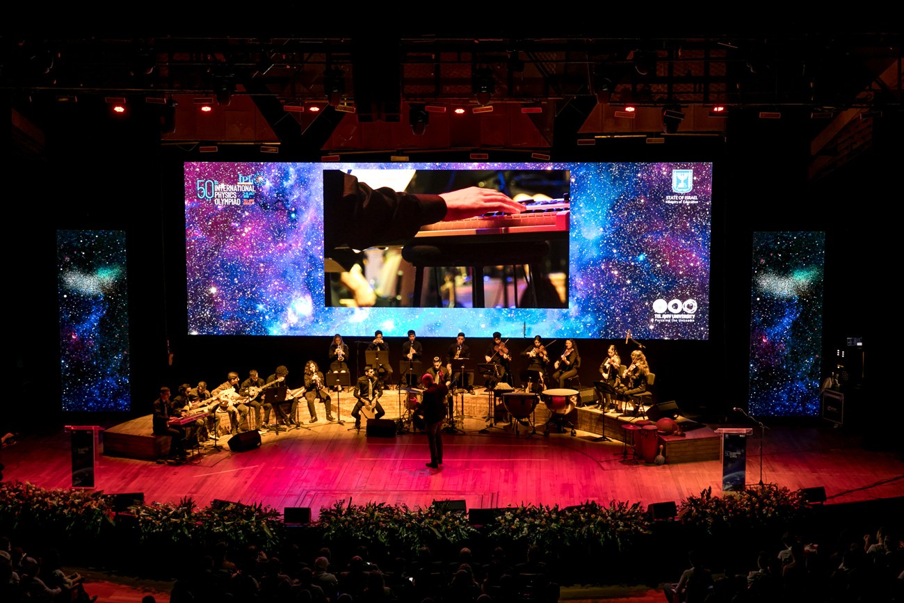 An orchestra on stage against a screen showing a night sky.