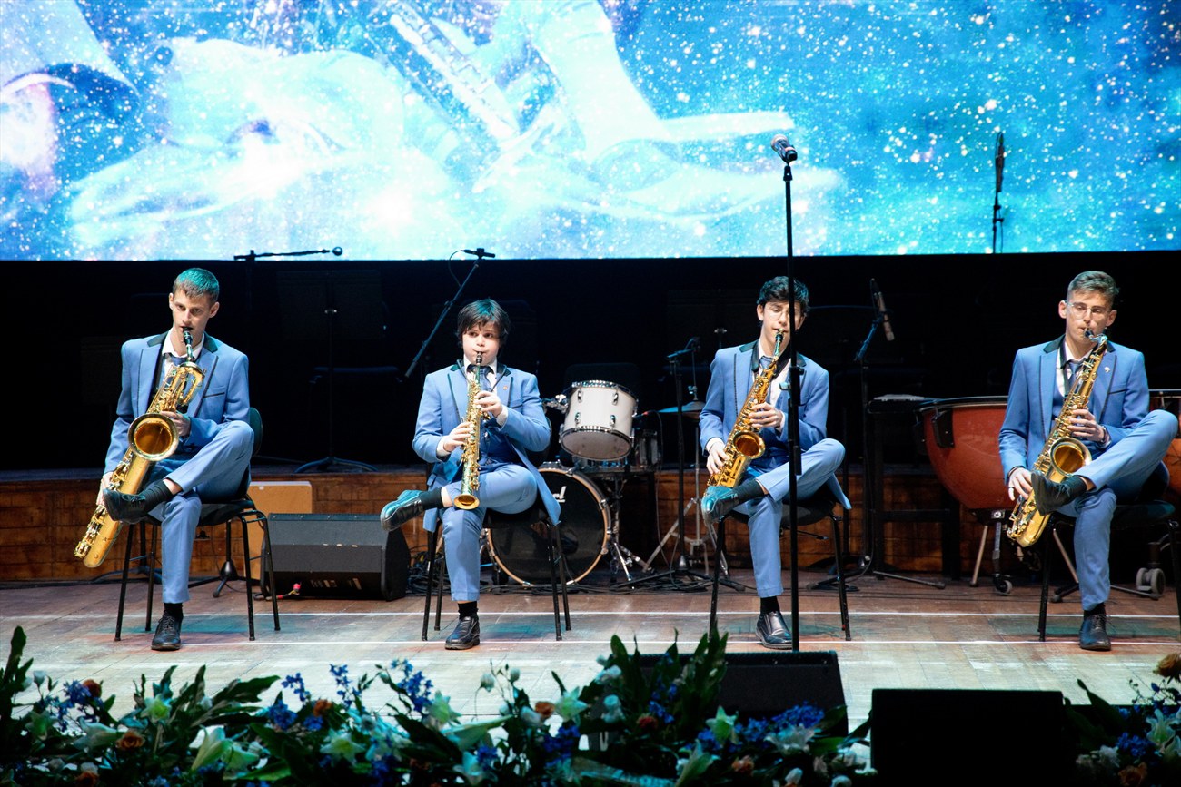 A saxophone quartet performing against a lit screen.
