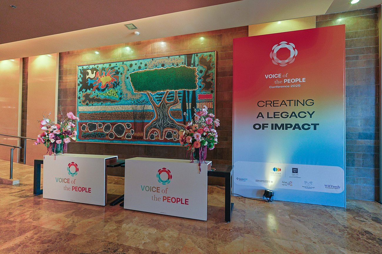 The entrance wall: a printed panel carrying the conference line beside an existing artwork, two branded desks and flowers in front of it.