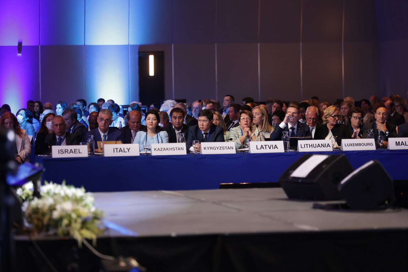 Delegates seated behind country nameplates reading Israel, Italy, Kazakhstan, Kyrgyzstan, Latvia, Lithuania and Luxembourg.